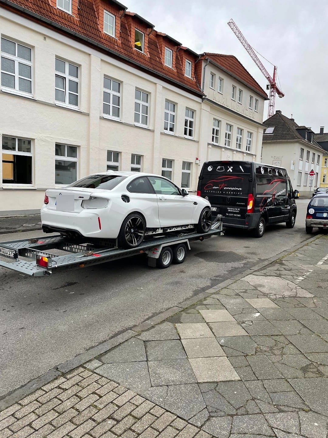 Transporter von Car Ferreira mit Autoanhänger, darauf ein weißer BMW M2, auf der Straße in Iserlohn